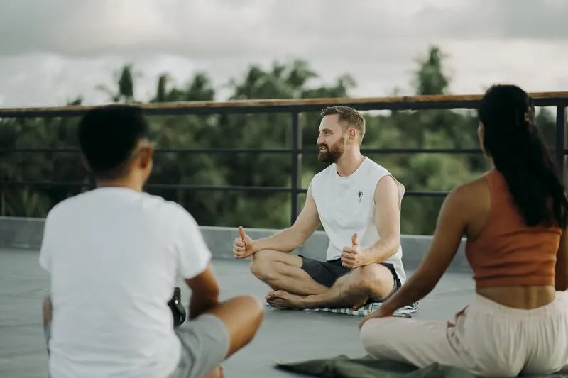 Timon Kukwa leitet im Schneidersitz eine Meditation mit einer kleinen Gruppe auf einer Dachterrasse