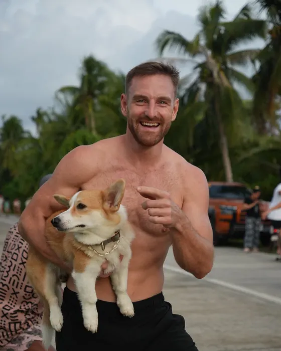 Timon Kukwa lacht und hält einen Corgi im Arm