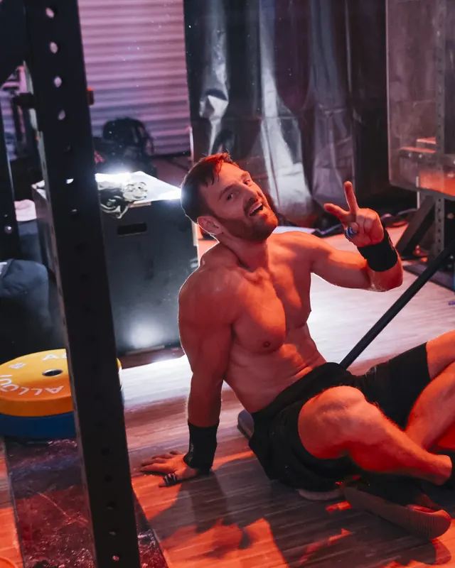 Timon Kukwa sitzt erschöpft nach einem Workout auf dem Boden eines Gyms in rotem Licht