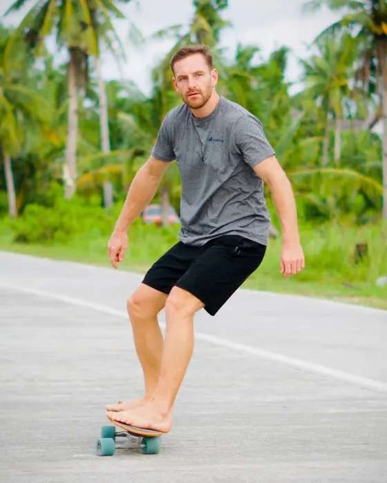 Timon Kukwa auf einem Surfskate auf einer Straße zwischen Palmen
