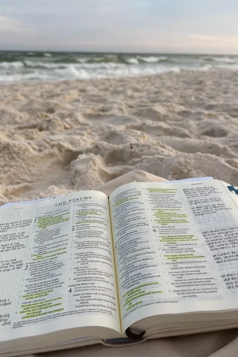 Eine aufgeschlagene Bibel mit handschriftlichen Notizen liegt im Sand, dahinter das Meer