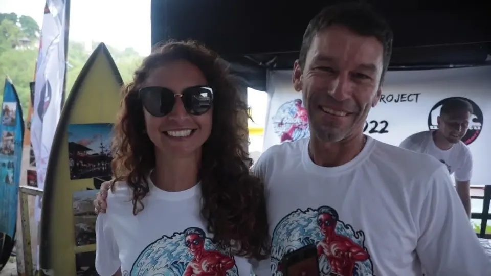 Zwei Menschen stehen lachend vor aufgestellten Surfbrettern