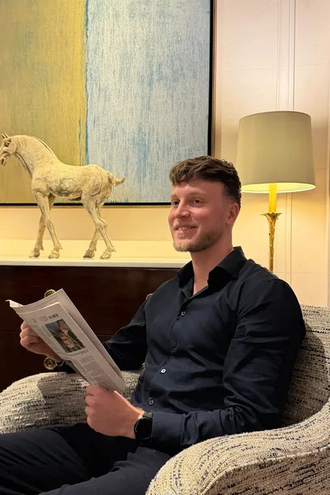 Janis Bachmann sitzt lächelnd mit einer Zeitung in einem Sessel einer Lounge