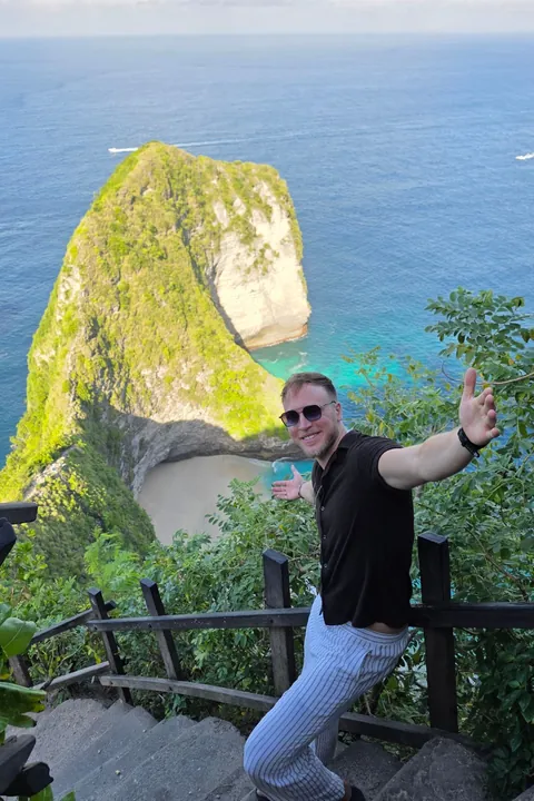 Janis Bachmann breitet auf einer Treppe an der Steilküste von Nusa Penida die Arme aus, hinter ihm Felsen und Meer