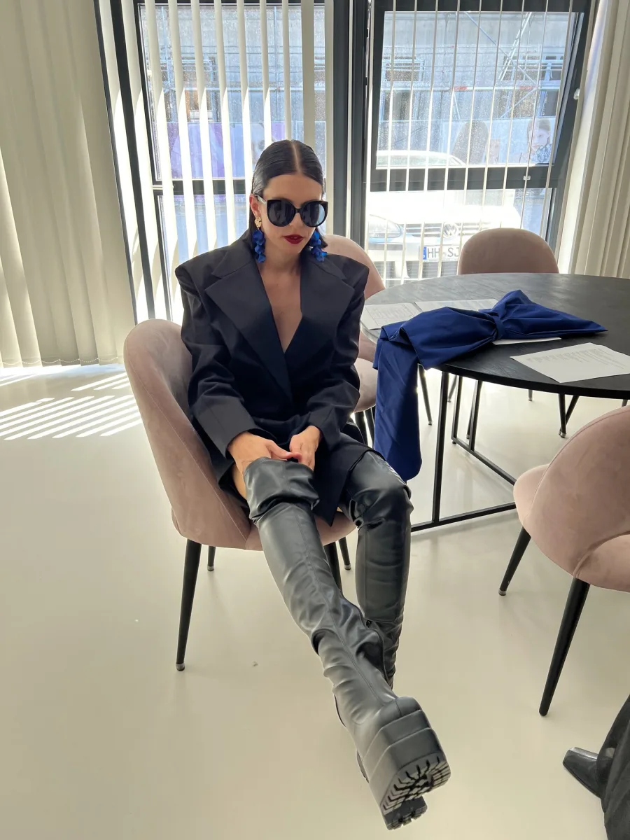 Sophia Elpel bei einem Modeshooting, sitzend mit Sonnenbrille, Blazer und hohen Stiefeln
